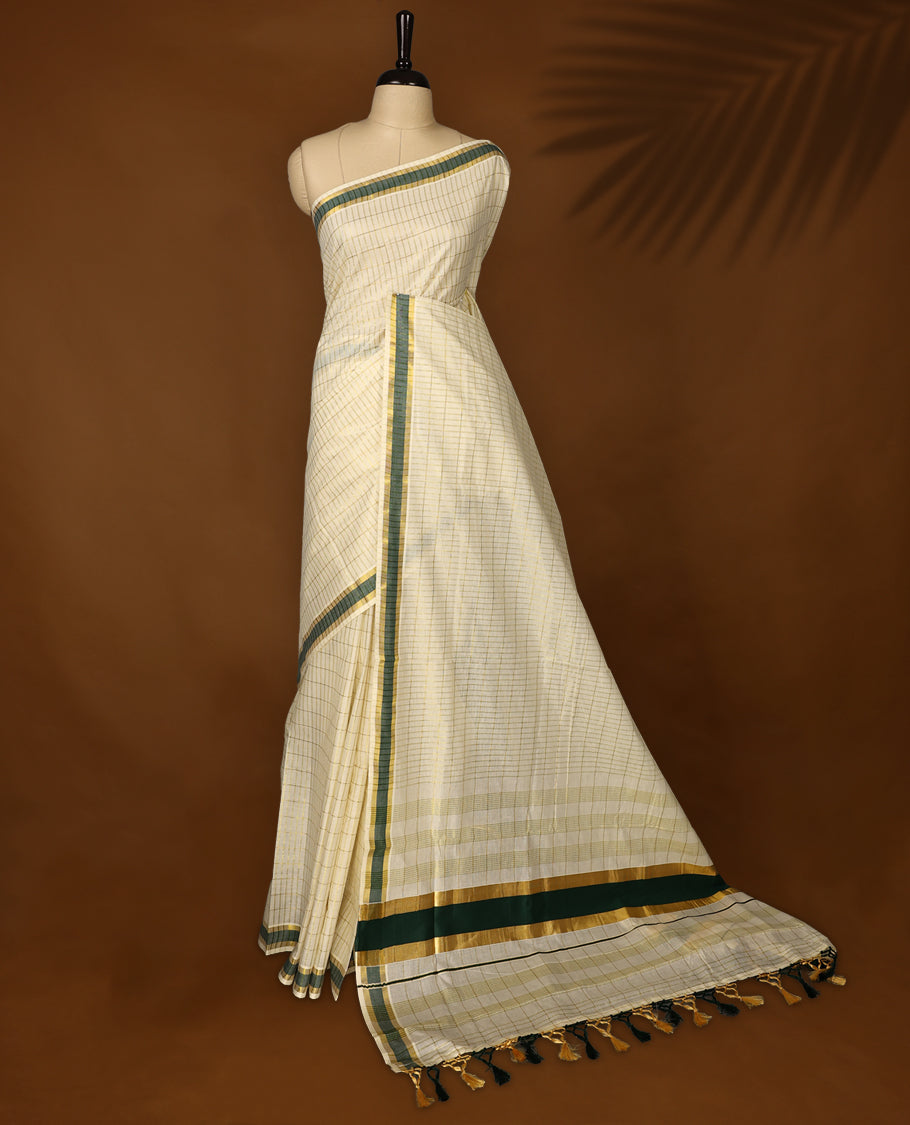 Elegant off white colour cotton Kerala saree featuring subtle golden checks, green & gold zari border, and rich striped pallu with tassels, offering a classic, graceful look &Pair with a matching blouse for charm.