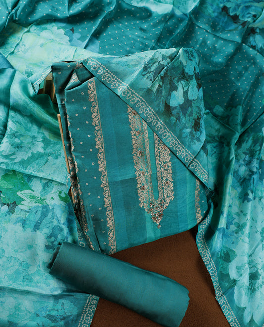 Teal green colour churidhar material adorned with intricate zari embroidery on the neckline, paired with a plain matching bottom and a floral printed dupatta highlighted with dotted accents.
