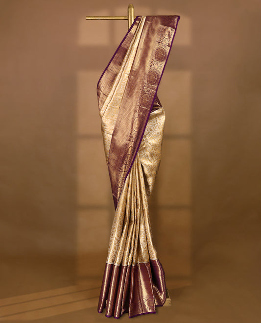 Gold colour tissue brocade saree with gold and silver zari floral pattern on body, gold zari traditional floral and chakkram work royal purple border, rich matching pallu with Antique zari motifs, paired with matching blouse.