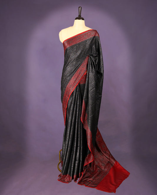 Black colour semi Banaras Katan saree featuring an antique zari jacquard body, complemented by a contrasting traditional border with a floral kodi design, paired with a matching blouse.
