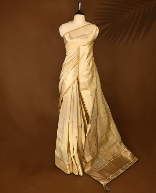 Light gold colour Organza Kerala saree featuring a luminous body with a subtle golden sheen, enhanced by a sleek zari border and scattered sequin like floral motifs, Paired elegantly with a matching blouse piece.