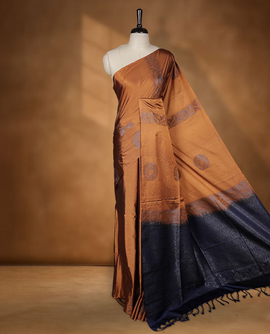 Mustard colour semi soft silk saree adorned with delicate woven floral kodi motifs on the body, complemented by a contrast navy blue colour woven pallu with intricate detailing and tassel accents without border & Comes with a matching blouse piece.