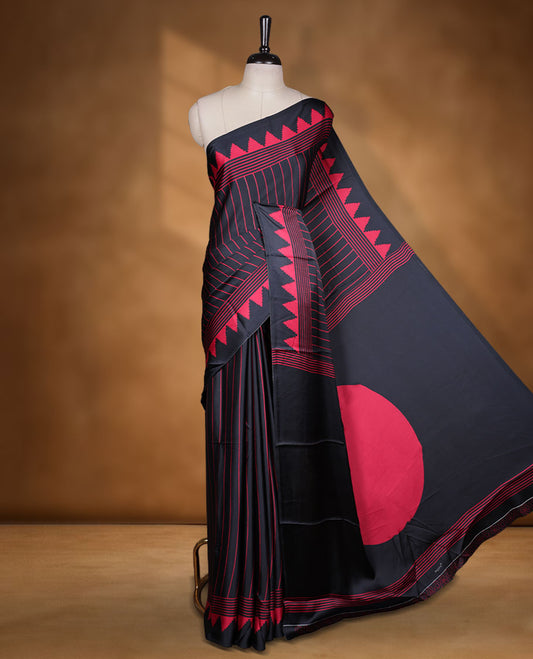 Black colour semi modal saree highlighted with red triangle border accents and sleek striped detailing across the drape, featuring a bold oversized red circular motif on the pallu, paired with a matching printed blouse.