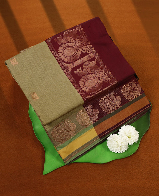 Olive Green and Maroon Kalyani cotton saree featuring subtle woven motifs on the body, accentuated with rich zari peacock designs on the border and pallu, paired with a matching blouse.