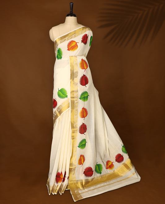 Elegant off white cotton Kerala saree adorned with vibrant multicolor leaf motifs, highlighted by a rich golden zari border and pallu paired with matching blouse.