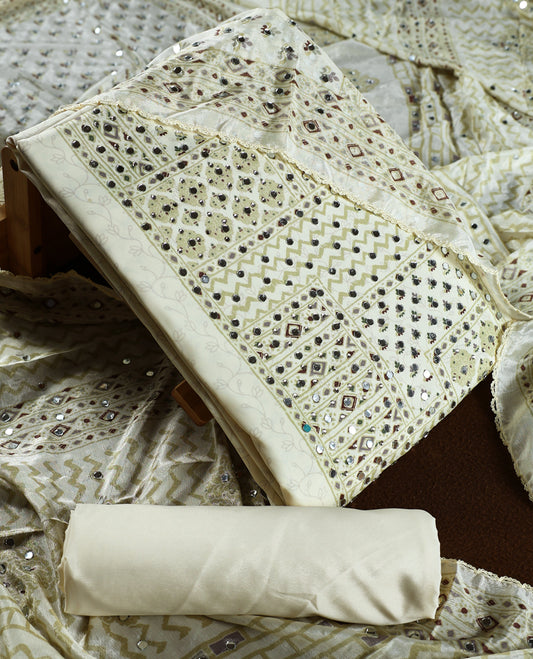 Cream colour churidar material adorned with intricate geometric designs and sparkling mirror work, paired with a plain matching bottom and dupatta.
