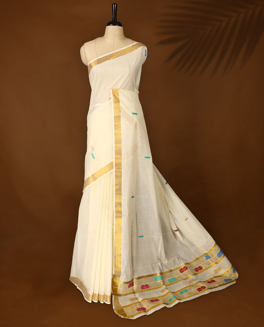 Elegant Off white colour cotton Kerala saree featuring colorful thread buttas and vibrant temple motifs on the pallu, finished with a classic golden zari border and paired with matching blouse.
