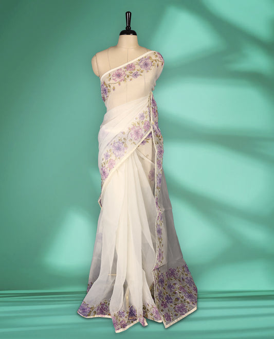 Ivory white colour organza saree adorned with purple floral print with thread detailing on the border and pallu, in a sheer finish that adds elegance, paired with a matching blouse for a graceful look.