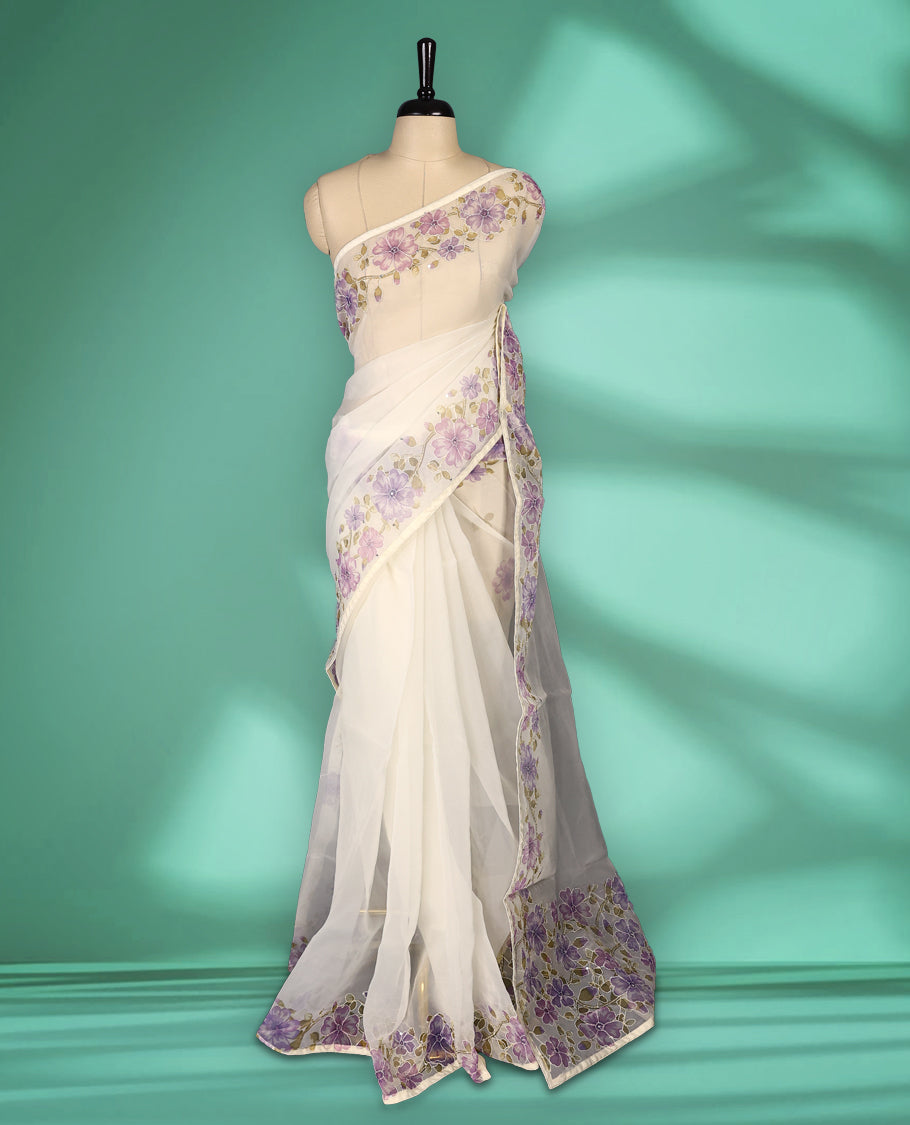 Ivory white colour organza saree adorned with purple floral print with thread detailing on the border and pallu, in a sheer finish that adds elegance, paired with a matching blouse for a graceful look.