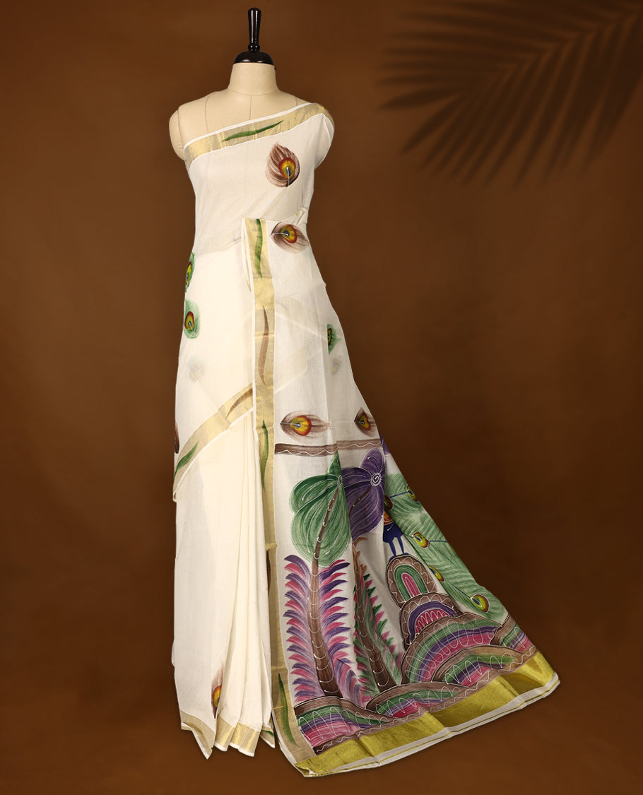 Elegant off white colour cotton Kerala saree with hand-painted peacock feathers and scenic pallu artwork, highlighted by a golden zari border and pallu, paired with a matching blouse for a graceful festive look.