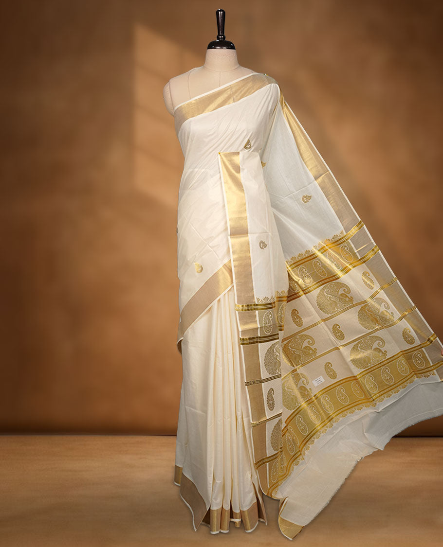 Off-white cotton Kerala saree with subtle gold zari buttas, a broad kasavu border, and a richly woven traditional pallu with paisley motifs. Paired with a matching plain blouse