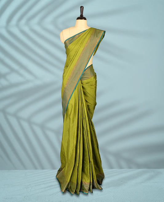 Olive green Colour semi silk saree showcases subtle golden thread checks and is beautifully complemented by a soft teal and gold zari border, paired with a matching blouse.