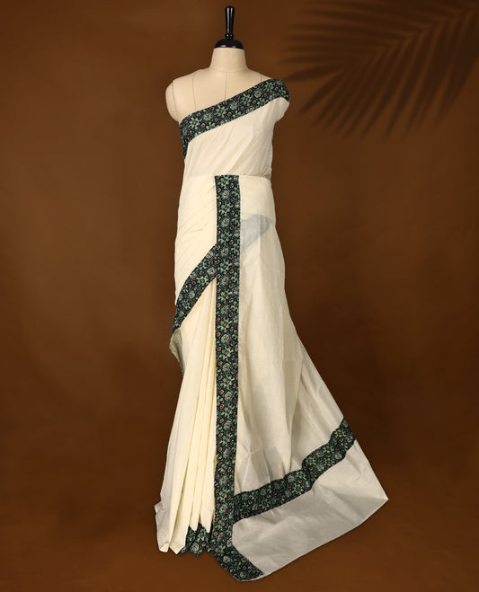 off white colour cotton Kerala saree adorned with a deep green border featuring intricate floral motifs in red and cream, paired with a matching printed blouse for a refined traditional look