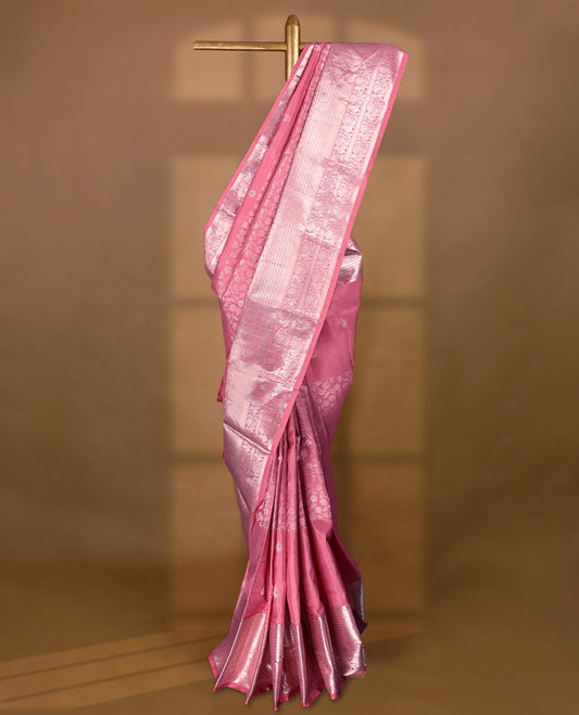 Light rose pink Colour traditional Kancheepuram silk saree adorned with antique zari small peacock motifs on the body, featuring a traditional border with light silver zari peacock and floral patterns, and paired with a matching blouse.
