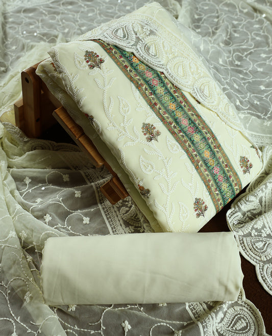 Cream colour churidhar material with embroidered green neck work, white thread floral motifs on the body, and multicolor detailing in green, pink & light brown &Comes with matching plain bottom and embroidered dupatta.