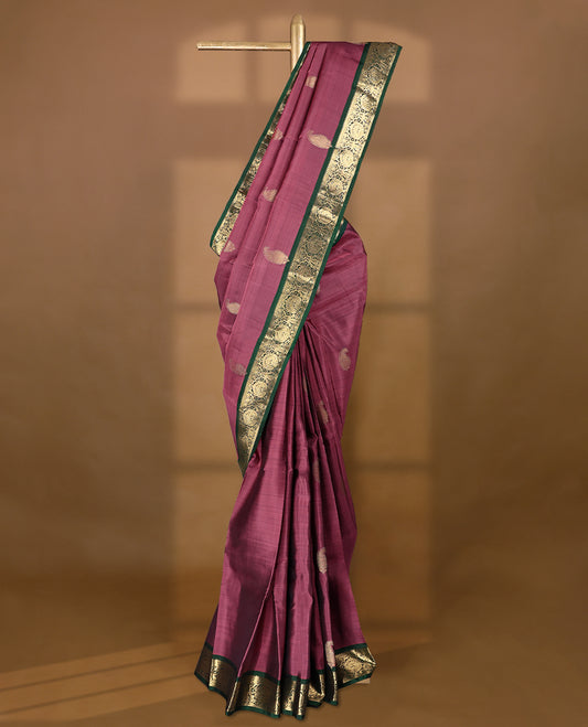 Solid mauve pink colour traditional Kancheepuram silk saree adorned with antique zari paisley motifs on the body, featuring a deep bottle green border with antique gold zari floral and vine patterns, and paired with a matching blouse.