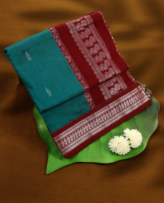Peacock Blue colour mixed Kalyani cotton saree featuring Silver zari peacock motifs throughout the body, paired with a Maroon colour traditional border and pallu, with matching blouse