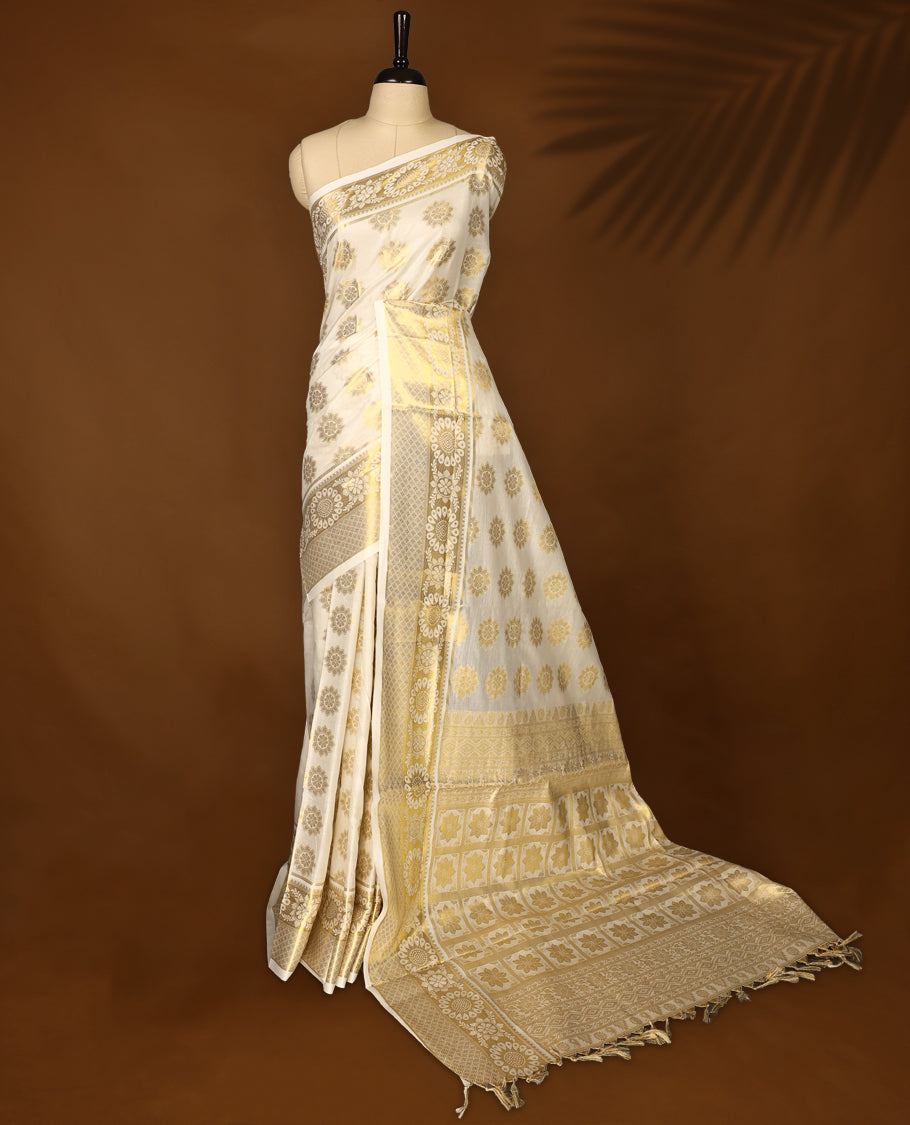 Elegant off white colour soft cotton Kerala saree adorned with golden floral motifs all over, accentuated by an ornate golden pallu with tassels, and a matching blouse, making it a perfect choice for traditional and festive celebrations.