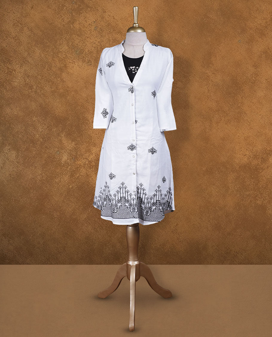 White embroidered shirt dress with band collar, contrast black inner layer at neckline, front button placket, three-quarter sleeves, and intricate black border embroidery at hem