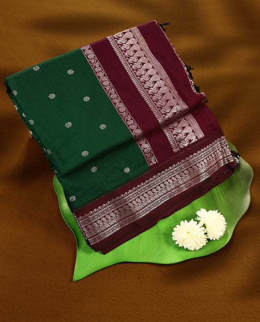 Bottle Green colour mixed Kalyani cotton saree featuring Silver zari flower motifs throughout the body, paired with a Maroon colour traditional border and pallu, with matching blouse