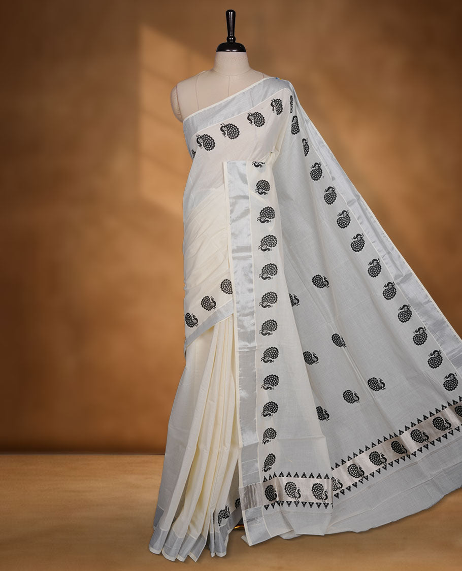 Off-white colour cotton Kerala saree featuring a subtle silver kasavu border, adorned with classic black peacock motifs across the body and pallu, and paired with a matching blouse.