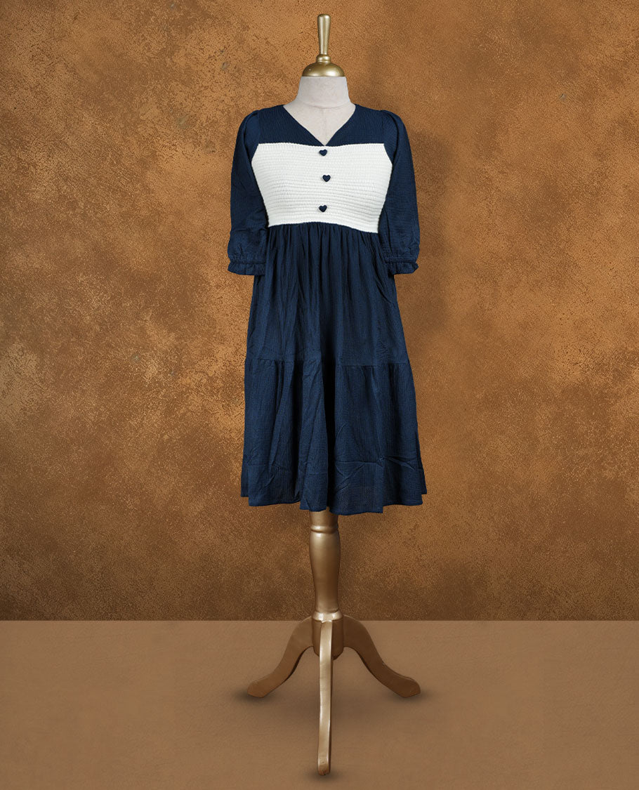 Navy blue knee-length tiered dress with V-neckline, contrast white textured yoke with button detail, and three-quarter puff sleeves.