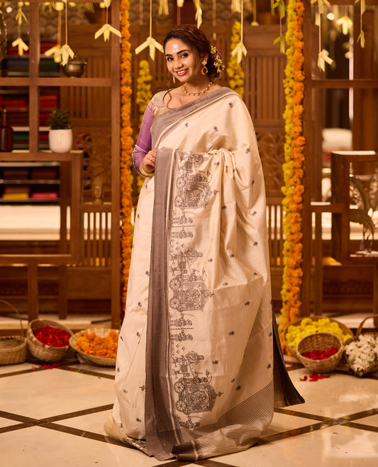 Off White colour Tussar saree adorned with small black woven motifs across the body, featuring an artistic temple chariot motif on the pallu, highlighted with a sleek grey border, paired with a matching blouse