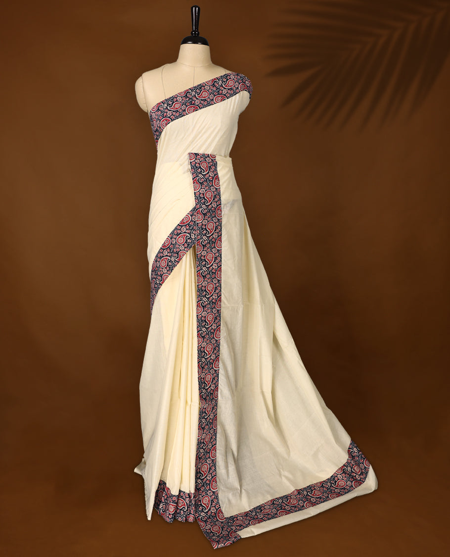 Off white colour cotton Kerala saree featuring a navy blue border with red and white paisley prints, paired with a matching printed blouse for a traditional yet vibrant look