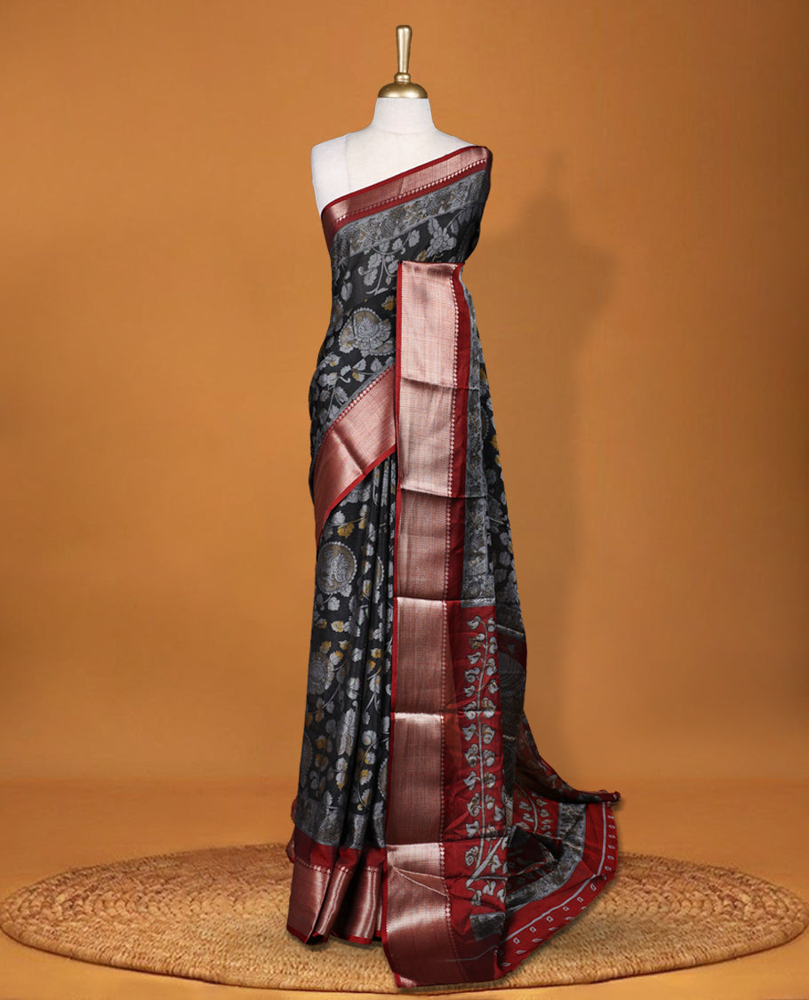 Black colour saree adorned with intricate floral motifs in subtle hues, featuring a rich maroon zari border and a beautifully woven contrasting pallu & Comes with a matching blouse piece.