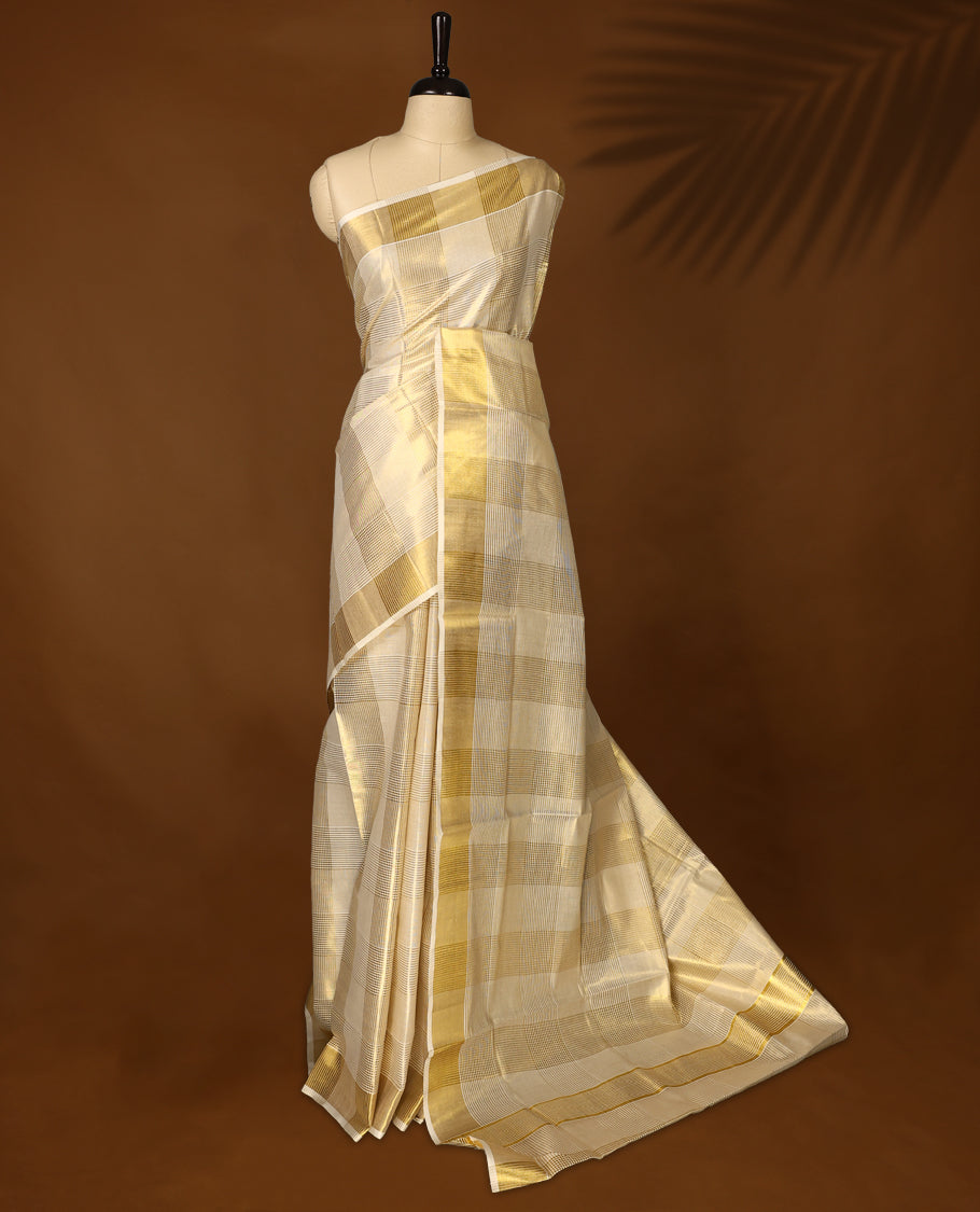 Elegant tissue Kerala saree with a cream base and golden checkered pattern, complemented by a rich golden zari border & Paired with a matching blouse, it's perfect for festive and traditional occasions.
