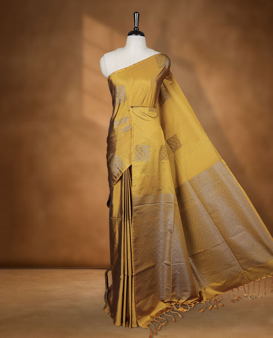 Olive yellow colour semi soft silk saree adorned with delicate woven floral in square motifs on the body, complemented by a Self colour woven pallu with intricate detailing and tassel accents without border & Comes with a matching blouse piece.