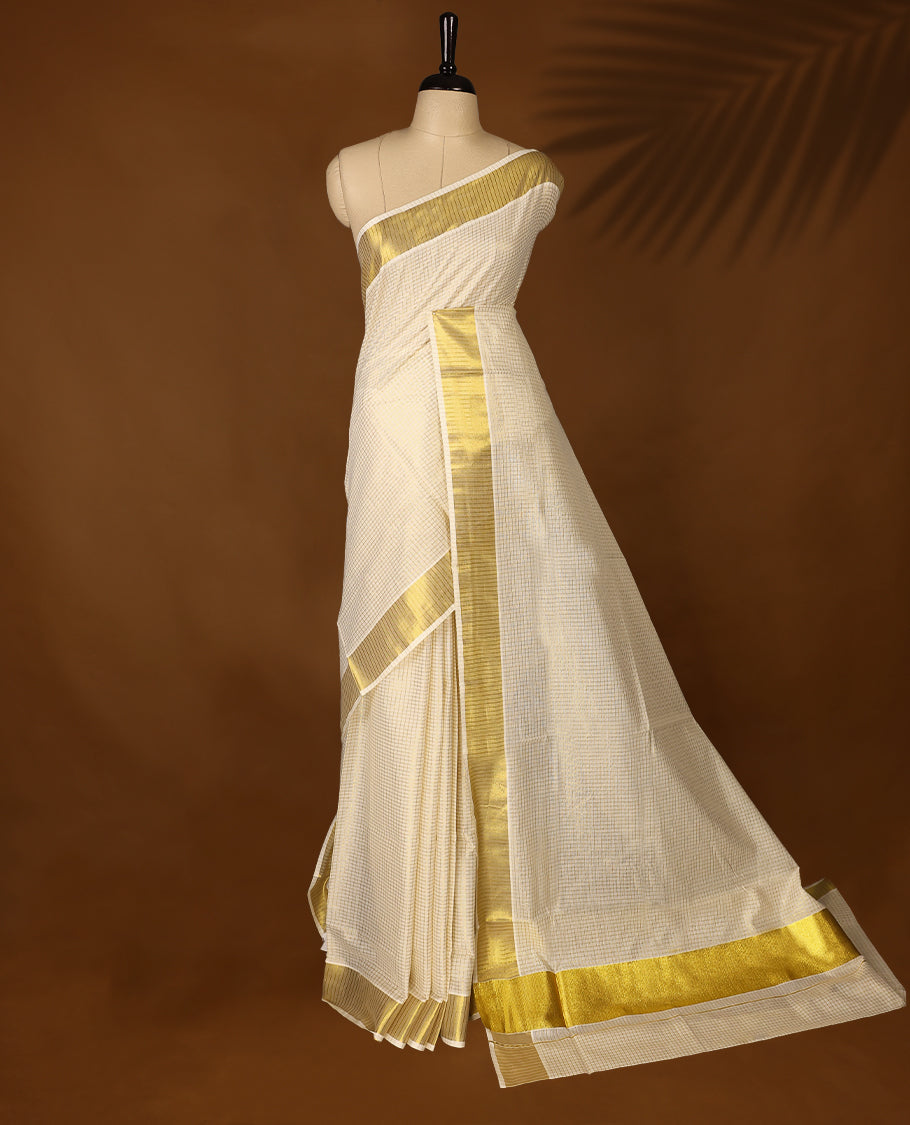 Elegant off white colour cotton Kerala saree featuring Tiny Checked body, gold zari traditional kasavu border offering a classic and graceful look, paired with a matching blouse.
