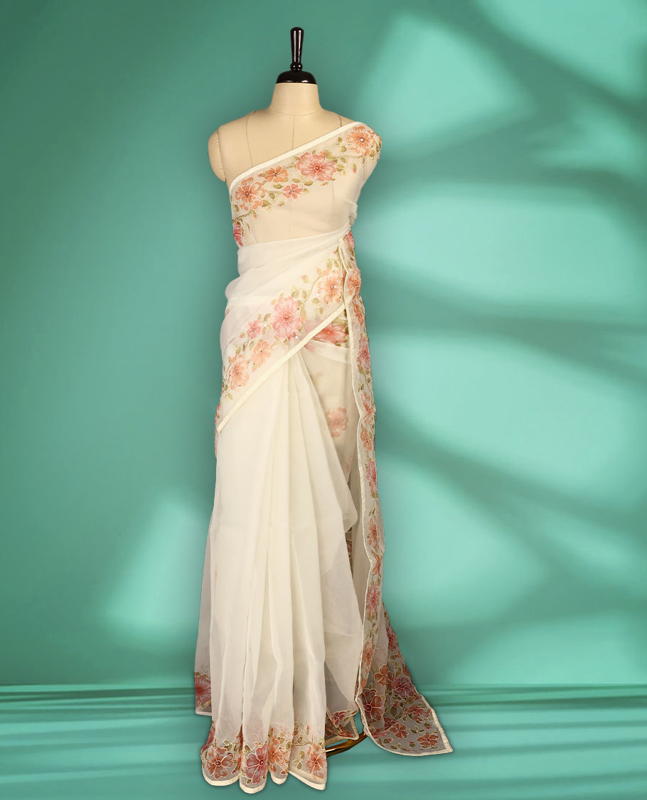 Ivory white colour organza saree adorned with Peach floral print with thread detailing on the border and pallu, in a sheer finish that adds elegance, paired with a matching blouse for a graceful look.