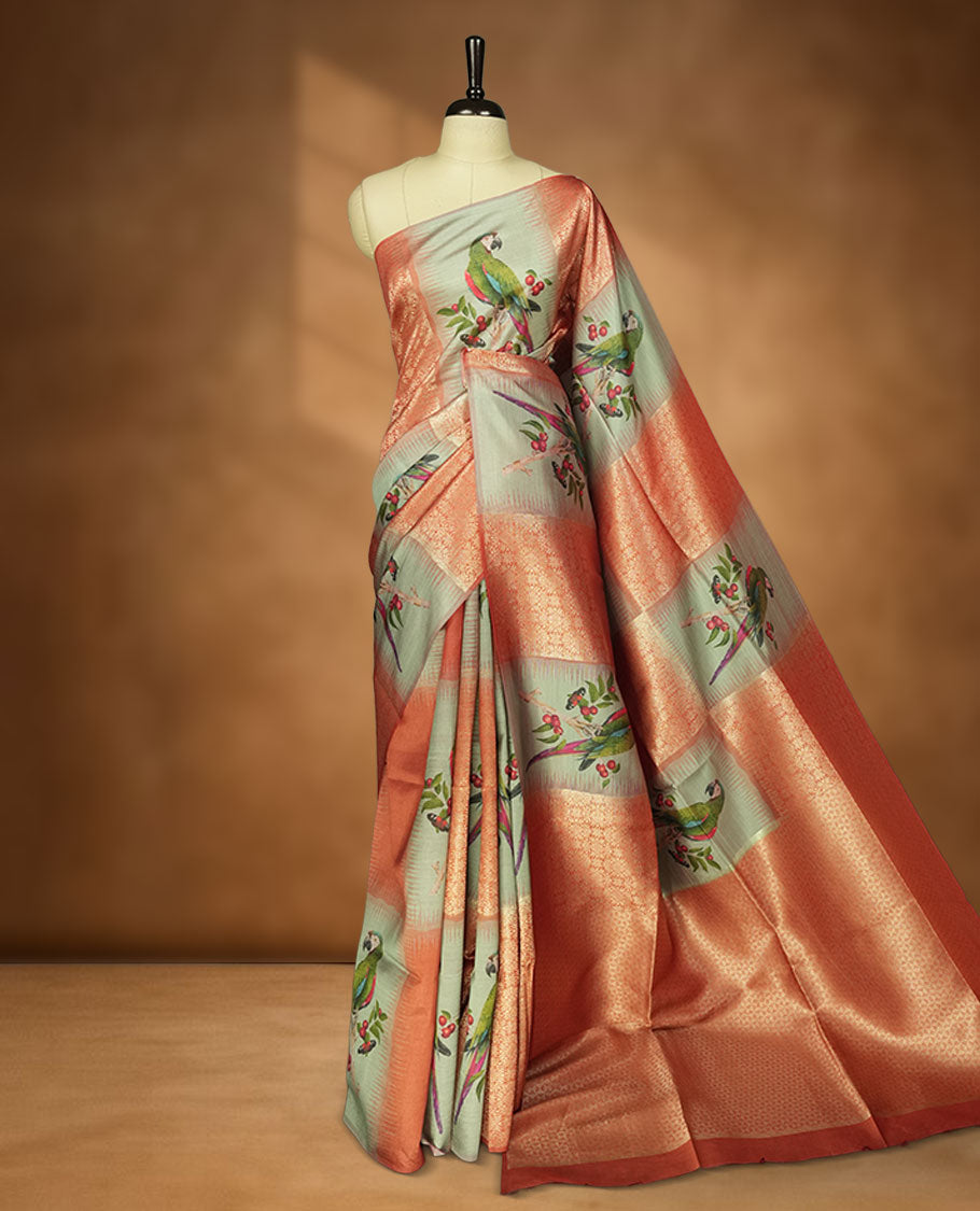 Peach and pastel green semi tussar Banarasi saree featuring artistic parrot prints perched on berry-laden branches across the body, with gold geometric woven patterns, an elegant peach zari border, and a matching blouse.
