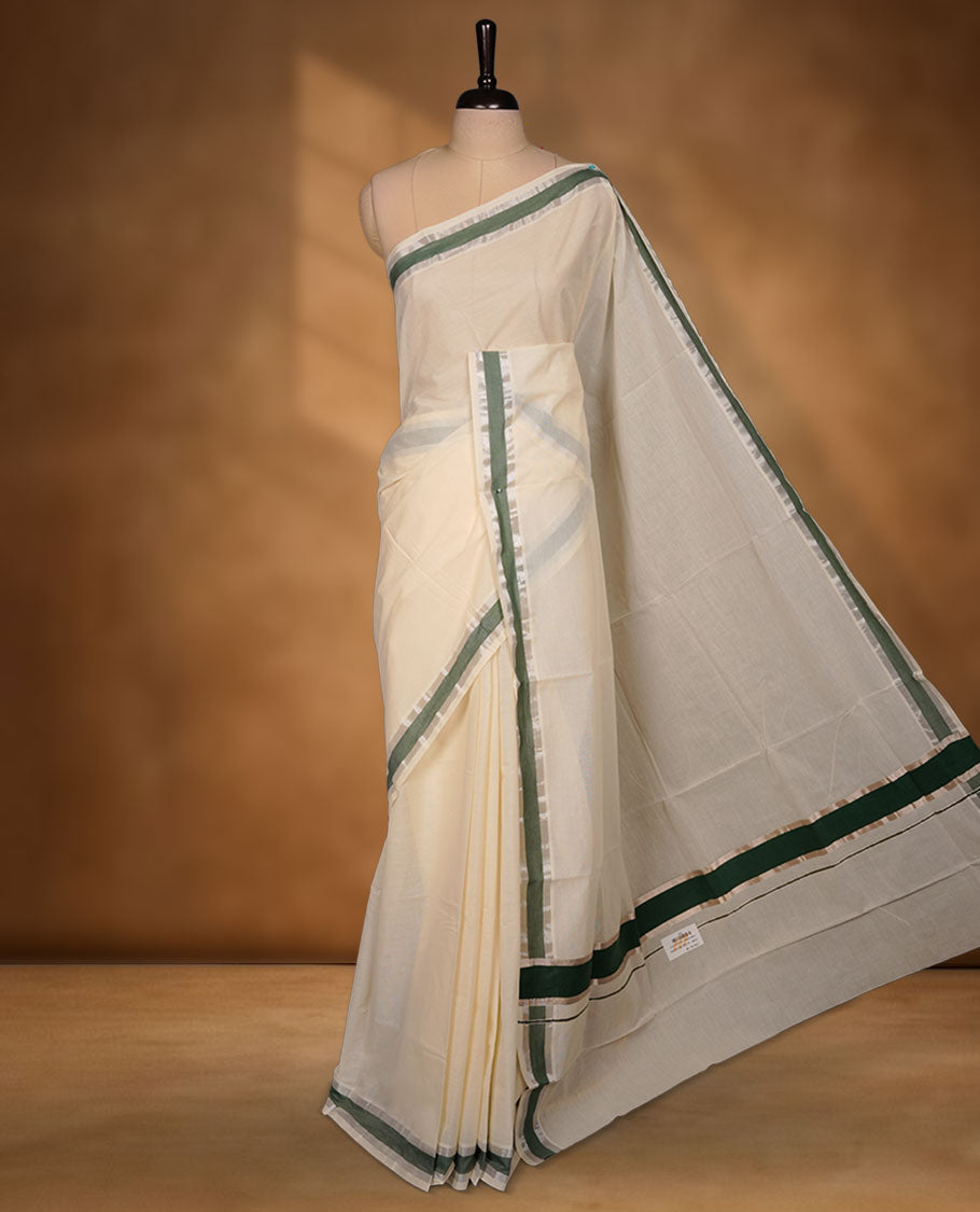 Off-white colour cotton Kerala saree featuring a subtle green border with silver zari accents, a clean plain body and pallu, and paired with a matching blouse.