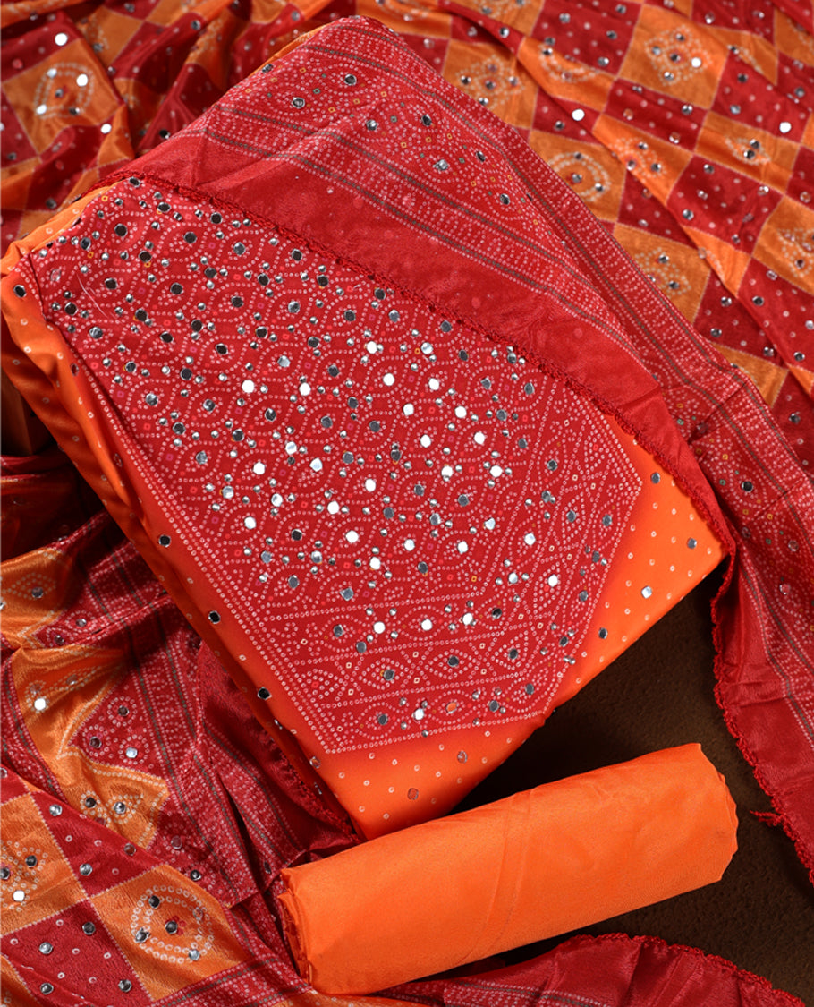 Red and orange colour churidhar material with intricate bandhani patterns and dazzling mirror work, paired with a plain matching bottom and vibrant dupatta, perfect for festive occasions and cultural celebrations.