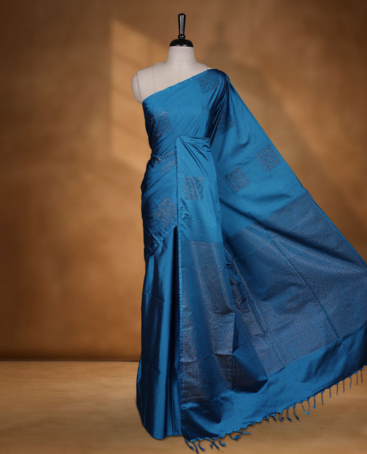 Ocean Blue colour semi soft silk saree adorned with delicate woven floral in square motifs on the body, complemented by a Self colour woven pallu with intricate detailing and tassel accents without border & Comes with a matching blouse piece.