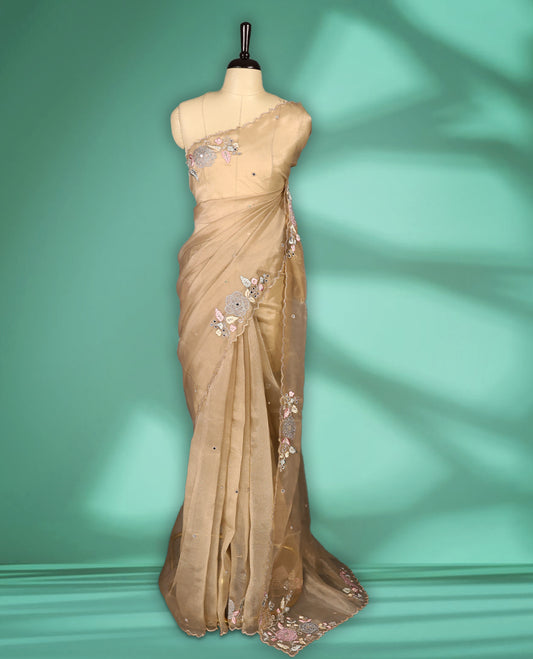 Dusty Pastel Brown colour organza saree featuring delicate floral embroidery with applique bead, mirror, and thread detailing on the body and scalloped border, lending a soft feminine charm, paired with a matching blouse.