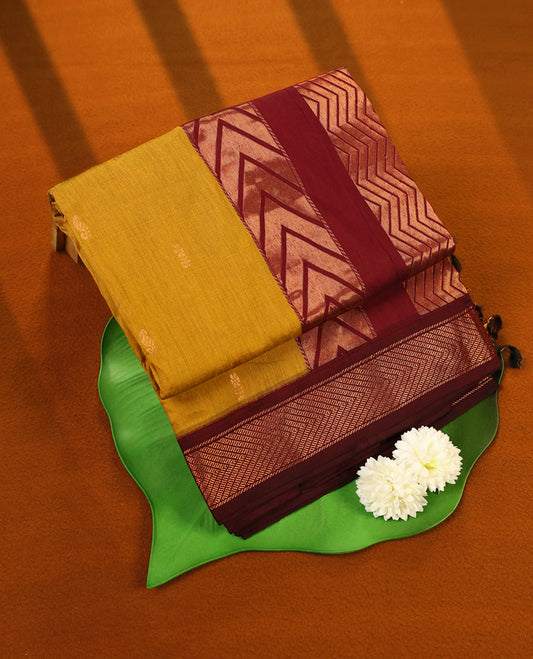 Mustard Yellow and Maroon Kalyani cotton saree featuring subtle woven motifs on the body, complemented by bold zig-zag patterned zari border and pallu, paired with a matching blouse.