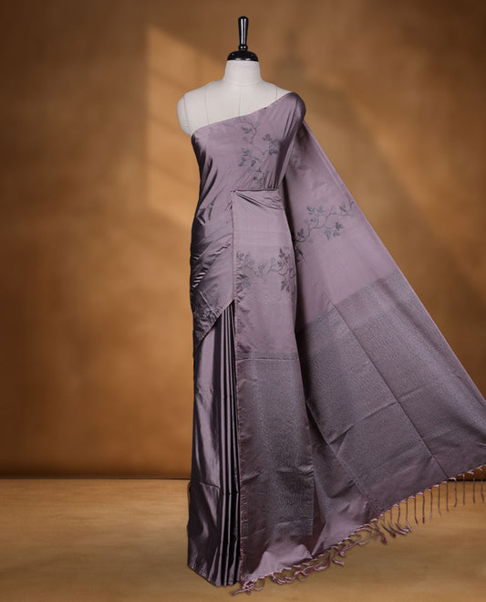 Pinkish gray colour semi soft silk saree adorned with delicate woven floral kodi motifs on the body, complemented by a Self colour woven pallu with intricate detailing and tassel accents without border & Comes with a matching blouse piece.