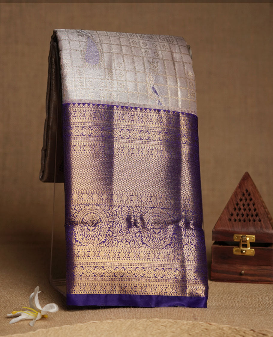 Cream Silk Saree with Purple & Gold Zari Checkered Grid Body, Textured Oval Buttas, Elegant Decorative Pallu Border, Grand Pallu with Ornate Peacock and Floral Motifs in Purple and Gold Tones, and Matching Purple Blouse.