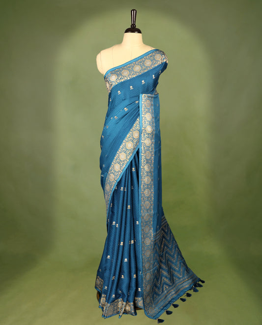 Blue colour pure Banaras crepe saree showcases elegant silver zari Flower Motifs all over the body, a traditional Banarasi gold zari border, a rich intricately woven pallu, and comes with a matching blouse.