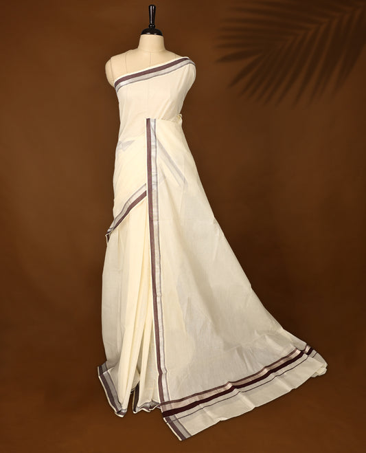 Classic off white colour cotton Kerala saree with elegant coffee brown and silver zari borders, exuding timeless charm. Paired with a matching blouse, perfect for traditional functions and cultural festivities.