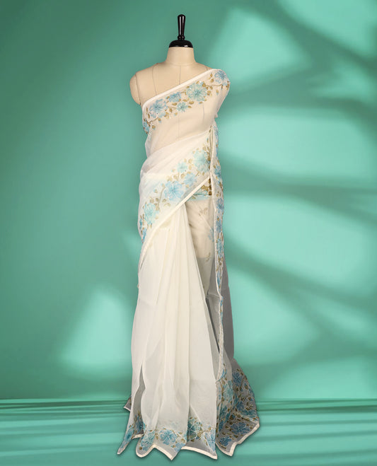 Ivory white colour organza saree adorned with aqua blue floral print with thread detailing on the border and pallu, in a sheer finish that adds elegance, paired with a matching blouse for a graceful look.