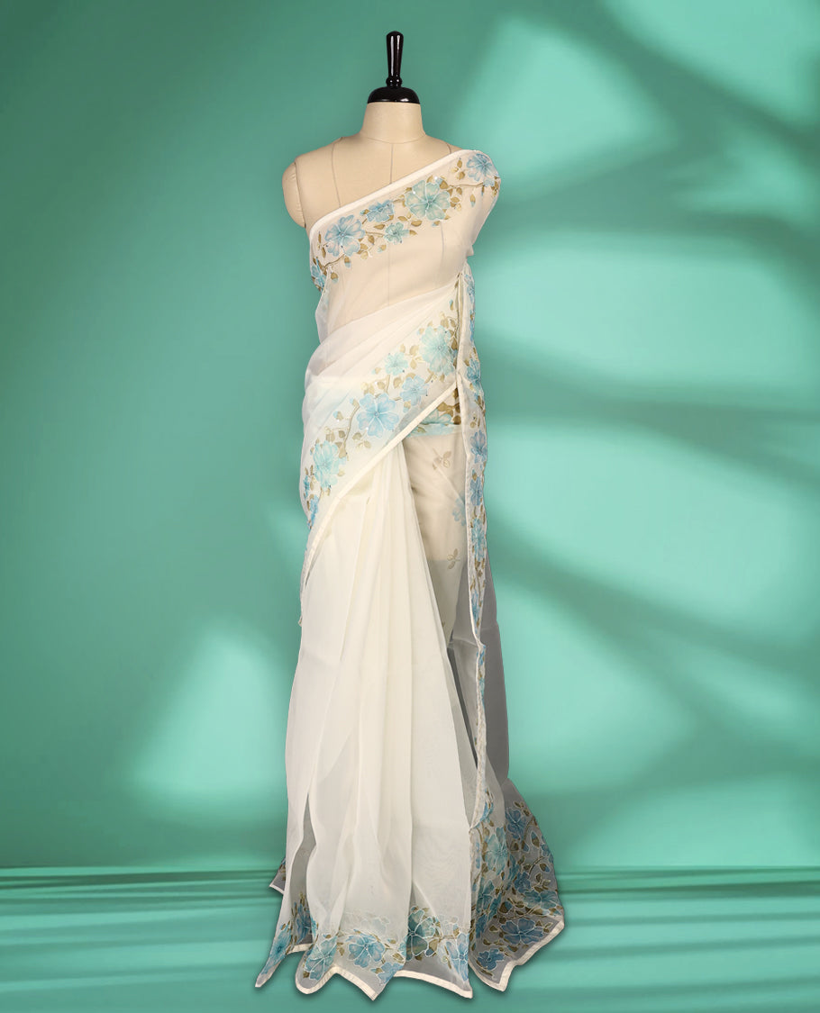 Ivory white colour organza saree adorned with aqua blue floral print with thread detailing on the border and pallu, in a sheer finish that adds elegance, paired with a matching blouse for a graceful look.