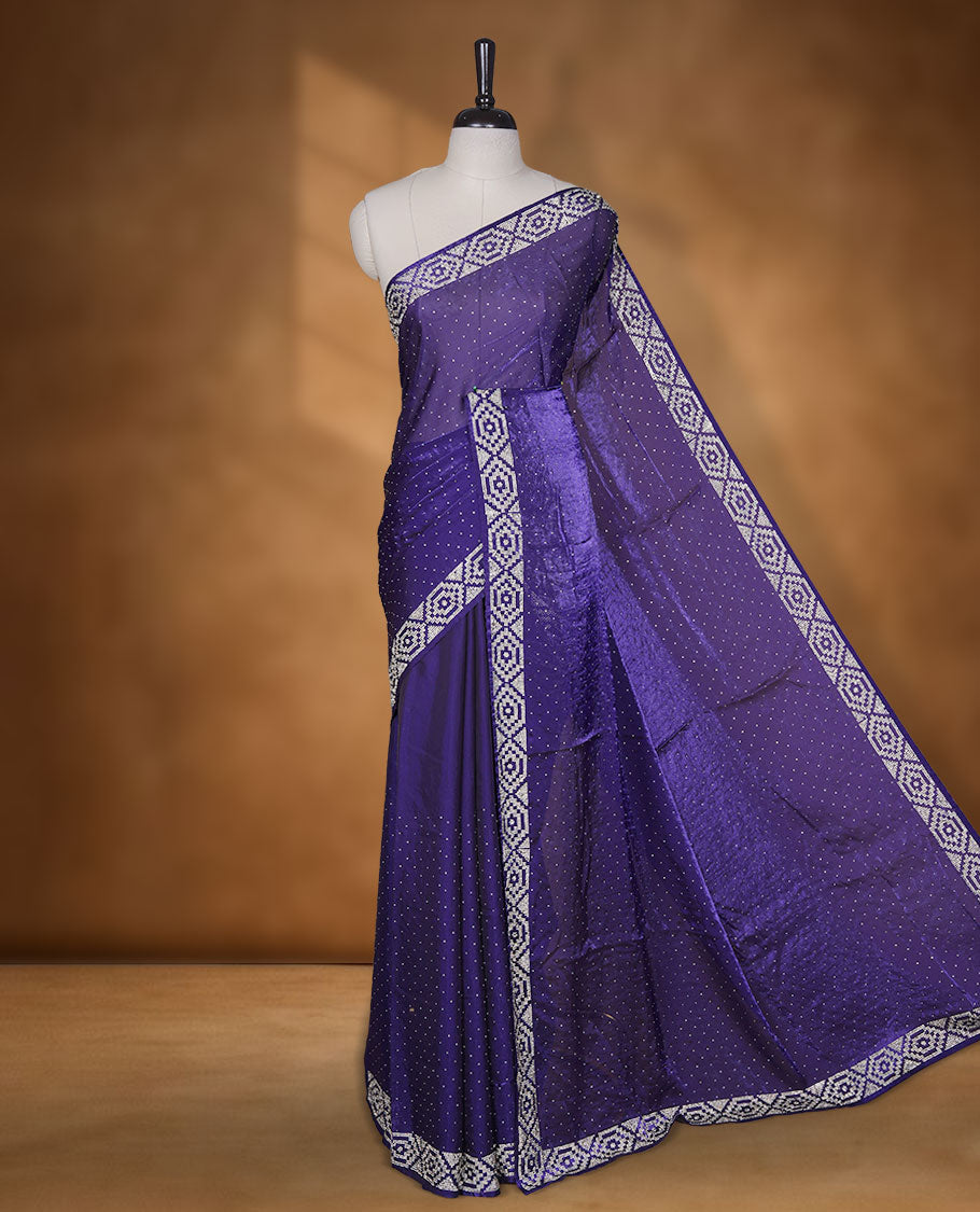Dark violet colour chiffon designer saree, featuring delicate scattered stone detailing all over the body, highlighted with intricate stone work and a heavy geometric stone pattern along the border and pallu, paired with a matching embellished blouse.a
