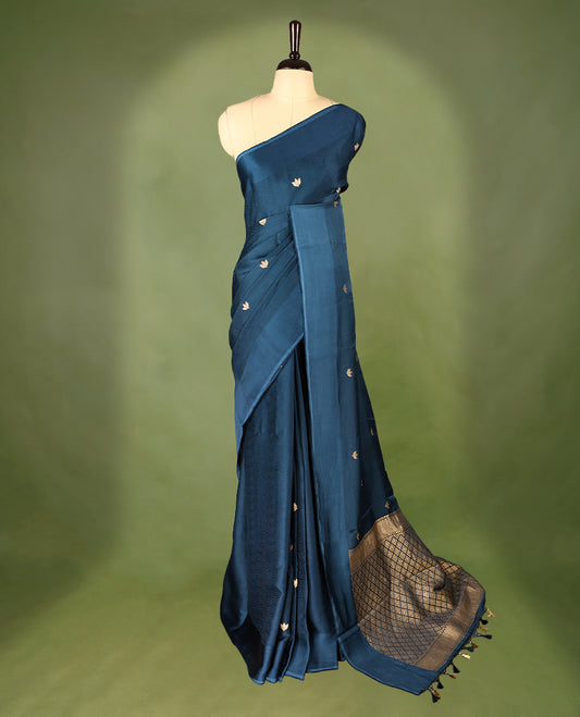 Deep teal colour crepe Banaras saree featuring small zari Floral Motifs across the body, without border, a sleek texture, and a rich golden zari pallu with geometric patterns, paired with a matching blouse for a graceful festive look