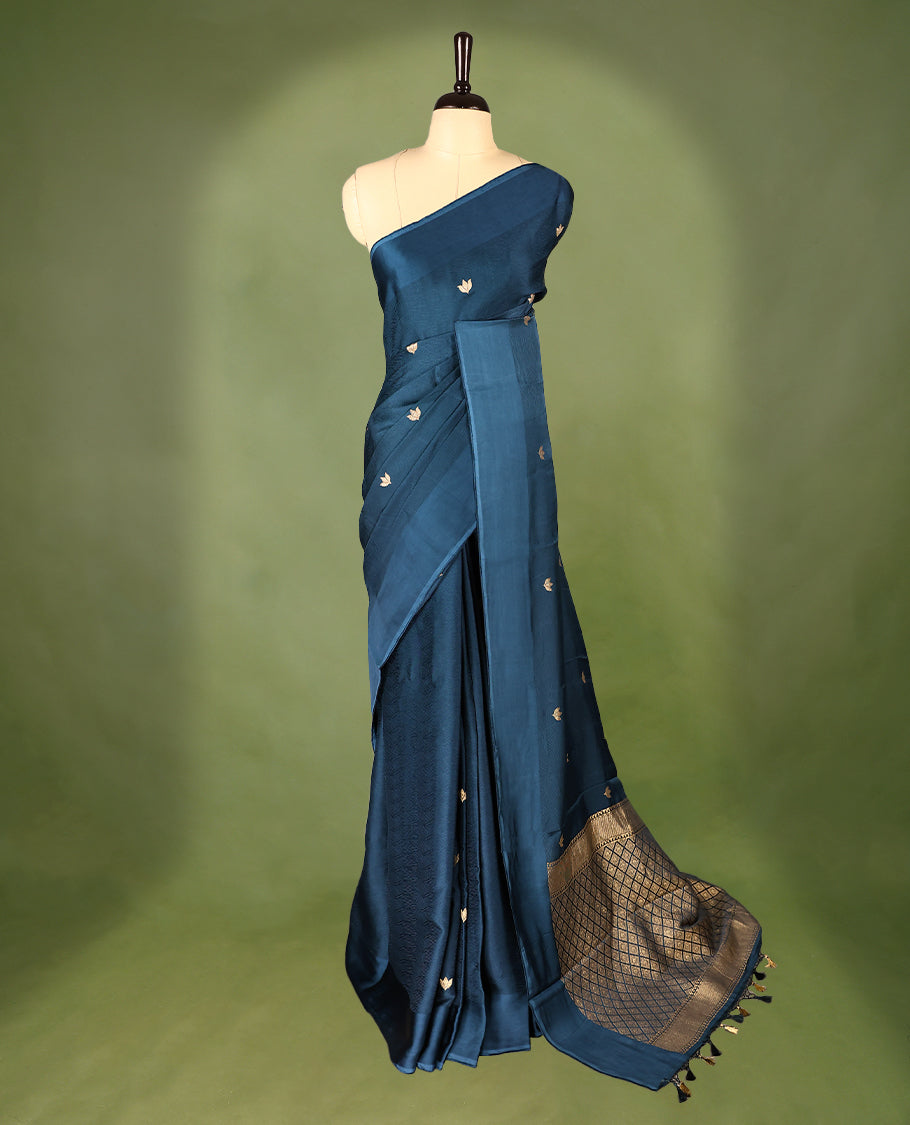 Deep teal colour crepe Banaras saree featuring small zari Floral Motifs across the body, without border, a sleek texture, and a rich golden zari pallu with geometric patterns, paired with a matching blouse for a graceful festive look