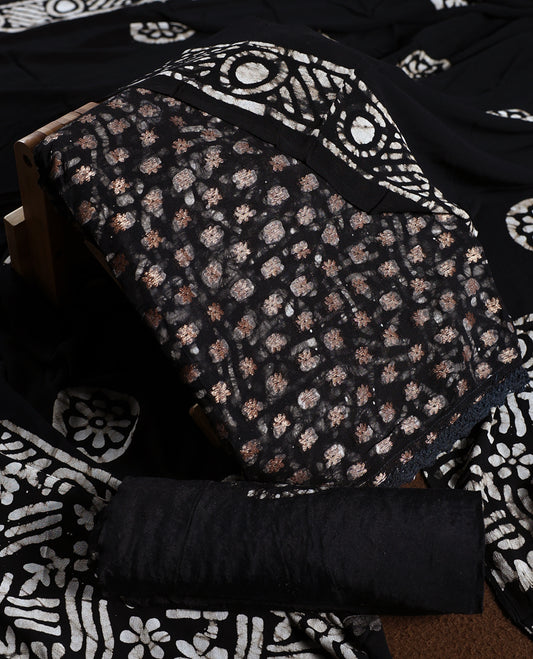 Black colour churidhar material adorned with gold and copper toned floral patterns and bold block designs, paired with a plain matching bottom and stylish dupatta, perfect for festive evenings and traditional gatherings.