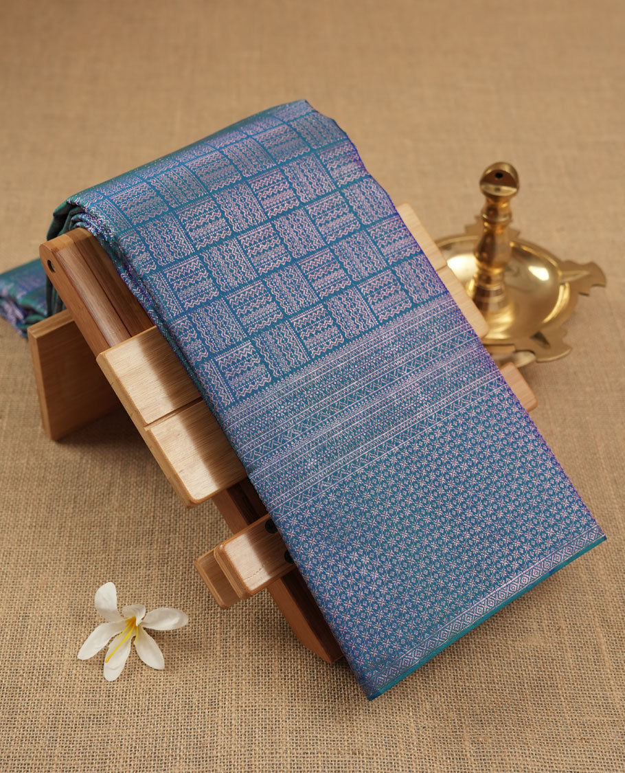Peacock blue colour Kanchipuram pattern Manthrakodi saree featuring intricate geometric antique copper zari brocade design across the body, beautifully complemented with a matching self brocade blouse piece.